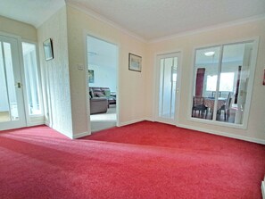 A spacious room with a red carpet, a dining area with a table and chairs, and a view through a glass door. - 4 bedroom accommodation in Carrbridge (Carrbridge)