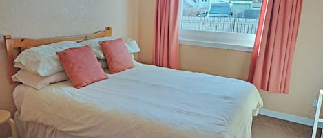 Una cama bien hecha con ropa de cama blanca y rosa, un cabecero de madera y un cuadro en la pared.