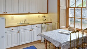 Una cocina con armarios blancos, encimera de madera, un fregadero, una tetera y una mesa de comedor con sillas.