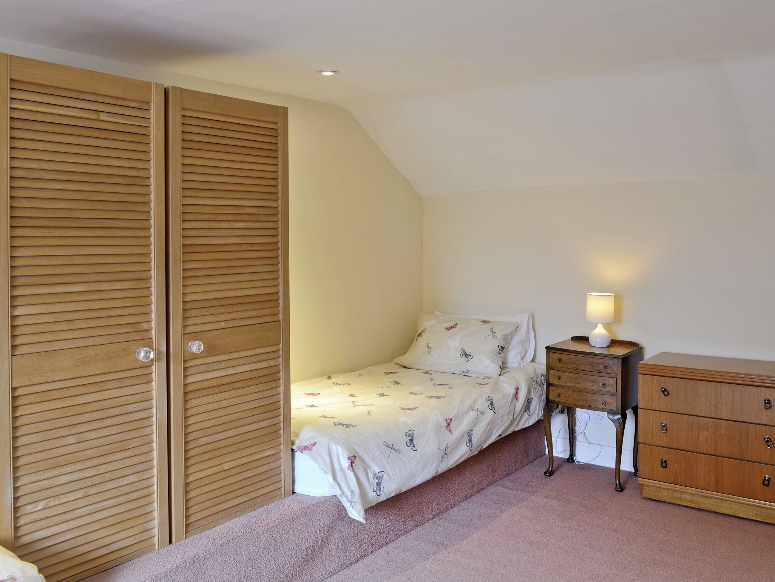 A bedroom with a bed, a nightstand, a dresser, and a wooden wardrobe.
