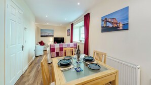 A dining area with a wooden table set for four, a sofa, and a TV in the background. - 2 bedroom accommodation in Stirling (Stirling)