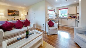 A modern living room with a sofa, armchairs, and a glass coffee table. A kitchen is visible in the background with a window and a sink. - 2 bedroom accommodation in Stirling (Stirling)