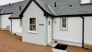 A row of single-story houses with grey roofs and white siding, featuring a small front porch and a window with a sign reading "Peregrine". - 2 bedroom accommodation in Stirling (Stirling)