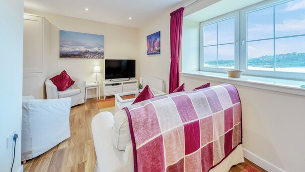 A modern living room with a flat-screen TV, a sofa, a chair, and a window with a view of a landscape. - 2 bedroom accommodation in Stirling (Stirling)