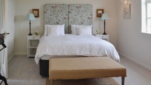 Una camera da letto ordinata con un letto grande, due comodini, una panca e uno specchio con carta da parati floreale.