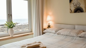 Une chambre à coucher avec un lit, une table de chevet avec une lampe, une fenêtre avec des rideaux et un tableau au mur.