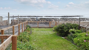 Un jardin en bord de mer, doté d’une terrasse en bois offrant une vue sur les côtes rocheuses et l’océan.