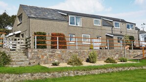 A two-story stone building with a sloped roof, a wooden fence, and a stone wall in front. - Fron Erch Cottages - 2712 (Abererch, near Pwllheli)