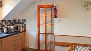 A kitchen with a microwave, kettle, and a wooden door. - Fron Erch Cottages - 2712 (Abererch, near Pwllheli)