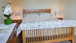 A bedroom with a wooden bed, floral bedding, two bedside lamps, a green vase with white flowers, and a wooden nightstand with a lamp. - Fron Erch Cottages - 2712 (Abererch, near Pwllheli)