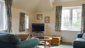 A living room with a sofa, a coffee table, a television, and a window with curtains. - 2 bedroom accommodation in Ambleside (Ambleside)