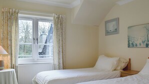 A bedroom with two single beds, a window with floral curtains, a bedside table with a lamp, and a painting on the wall. - 2 bedroom accommodation in Ambleside (Ambleside)