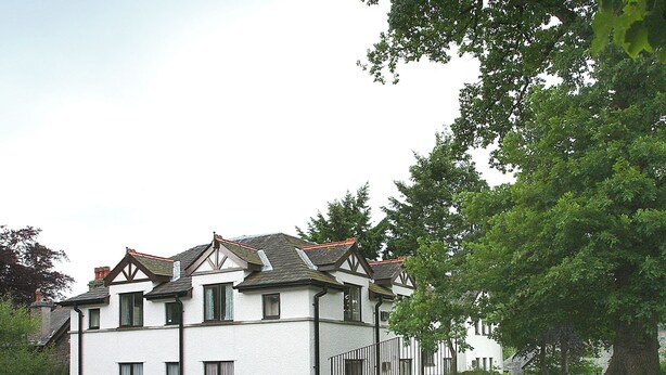 A two-story building with a white facade and dark trim, featuring a steeply pitched roof and multiple windows. - 2 bedroom accommodation in Ambleside (Ambleside)