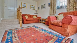 A living room with two sofas, a patterned rug, a staircase, and a bookshelf. - 2 bedroom accommodation in Birnam, near Dunkeld (Birnam, near Dunkeld)