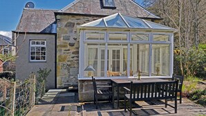 A stone house with a conservatory, a small window, and a table with chairs outside. - 2 bedroom accommodation in Birnam, near Dunkeld (Birnam, near Dunkeld)