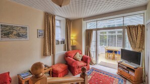 A living room with a red sofa, a television on a wooden stand, and a patterned rug. - 2 bedroom accommodation in Birnam, near Dunkeld (Birnam, near Dunkeld)