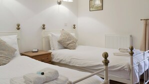 Une chambre d’hôtel avec deux lits simples, une table de chevet avec une lampe, un tableau encadré au mur et un radiateur.
