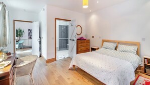 A bedroom with a bed, wooden dresser, and a desk with chair. There is a bathroom with a shower and a mirror.