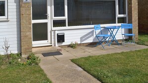 A house with a number 2 sign, a large window, and a small patio with blue chairs.