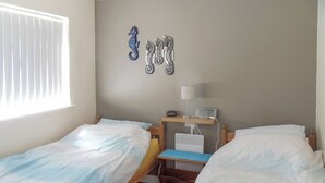 A room with two beds, a bedside table with a lamp, a small shelf with a radio, and a wall-mounted heater.