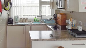 A kitchen with a sink, countertop, and cabinets. There are utensils and a coffee maker on the counter.