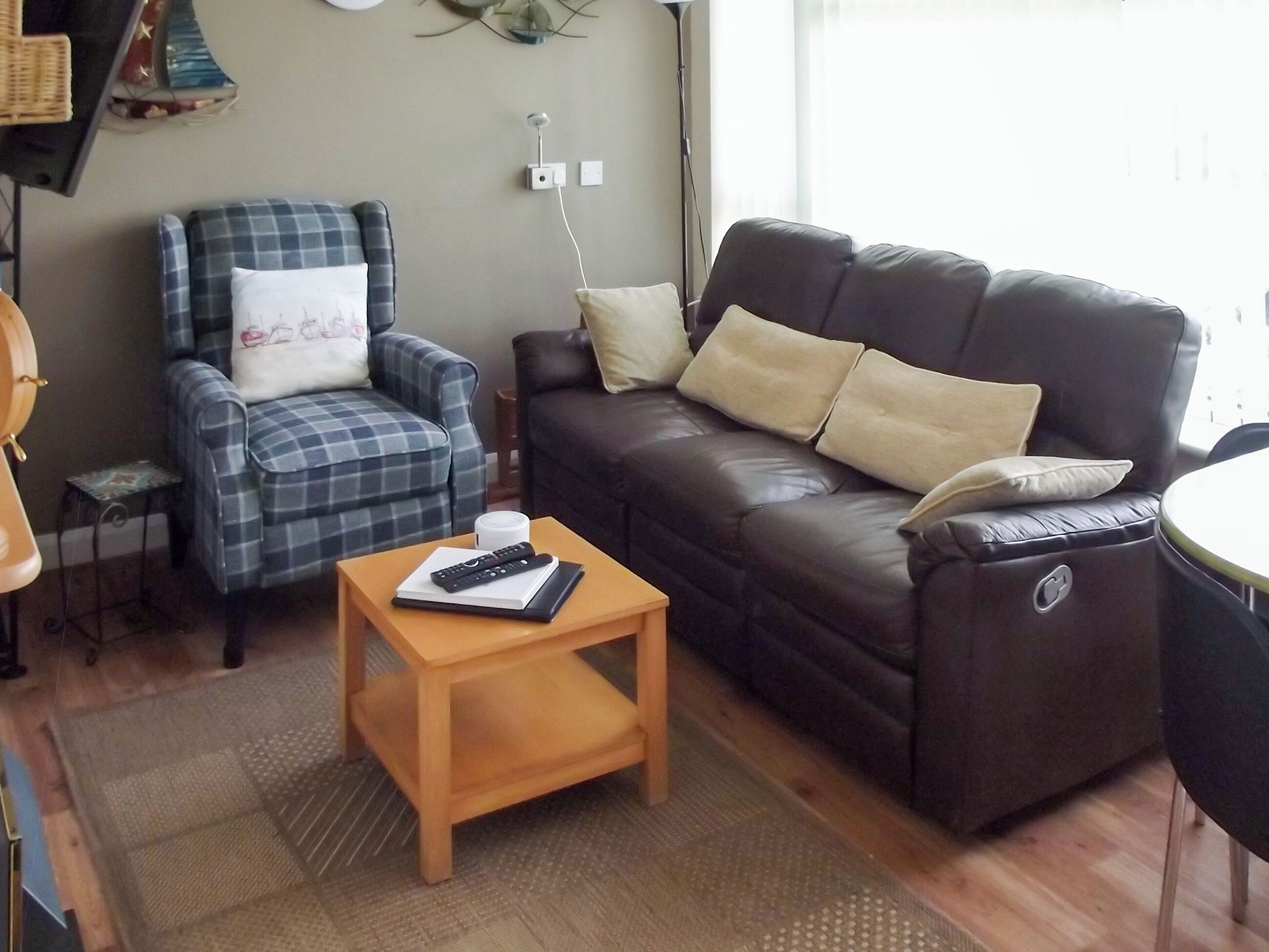A living room with a blue plaid armchair, a black leather sofa, and a wooden coffee table with a remote control.