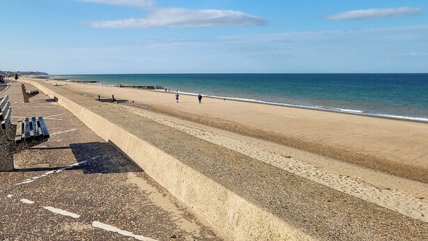 A beach with a concrete walkway, benches, and a clear view of the sea.