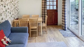 Una sala de estar acogedora con un sofá azul, una mesa de comedor con sillas, una puerta de madera y un amplio ventanal con cortinas.