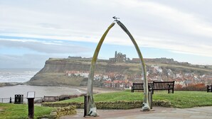 A coastal town with a historic castle on a hill, benches, and a stone pathway.