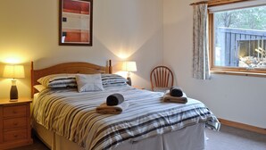 A neatly made bed with striped bedding, two bedside lamps, a wooden nightstand, a chair, and a window with curtains.