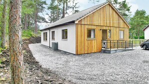 A wooden cabin with a gravel driveway, surrounded by trees.