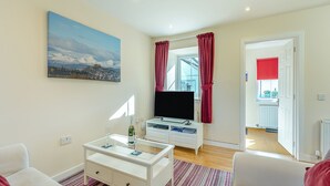 A modern living room with a flat-screen TV, a glass-top coffee table, and a painting on the wall. - Kestrel Cottage - 27937 (Stirling)