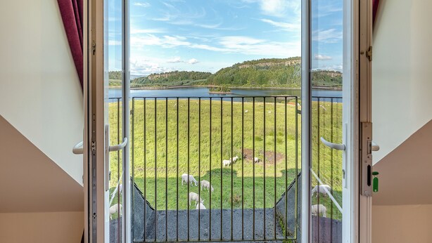 A balcony with a metal railing, a grassy field, and a lake in the background. - Kestrel Cottage - 27937 (Stirling)