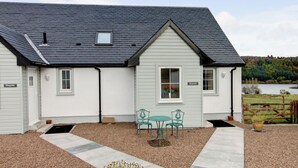 A house with a grey roof, white exterior walls, and a small window. There is a table and two chairs in front of the house. - Kestrel Cottage - 27937 (Stirling)