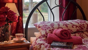 A neatly made bed with a floral-patterned bedspread, a rolled towel, and a book titled "The Pagan Lord" on the bedside table.