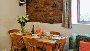 Zona pranzo con parete in pietra, tavolo di legno, sedie e finestra con tende.