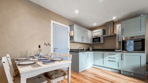 Una cocina moderna con armarios blancos, una mesa de comedor para cuatro personas y suelo de madera.