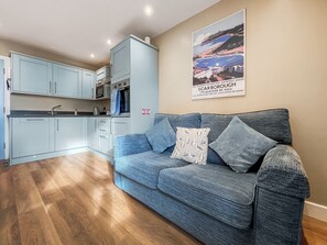 A modern living room with a blue sofa, wooden flooring, and a kitchen area with light blue cabinets.