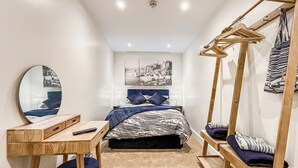 Un dormitorio con cama, escritorio, silla, perchero y espejo.