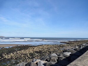 A rocky shoreline with waves, a clear sky, and a distant view of the ocean.
