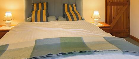 A neatly made bed with striped pillows and a checkered blanket, flanked by two bedside lamps on wooden nightstands.