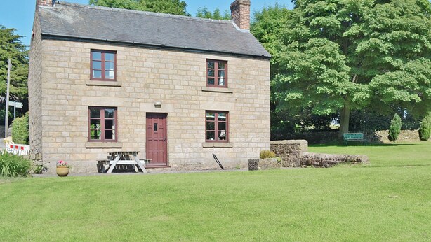 A stone building with a red door and windows, surrounded by a grassy lawn and trees. - A detached farmhouse with views down the Derwent Valley. (Crich)