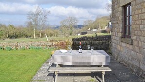 Een picknicktafel buiten een stenen gebouw, met een geruit tafelkleed, een fles en glazen.