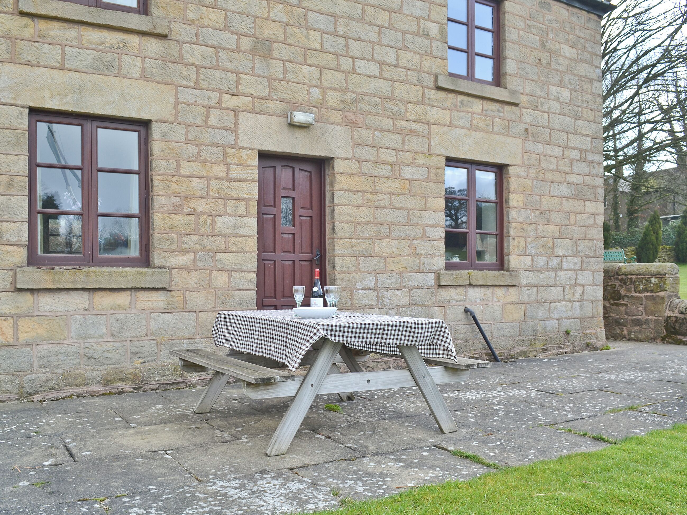 Un bâtiment en pierre avec une table à carreaux et des verres à vin placés à l’extérieur.