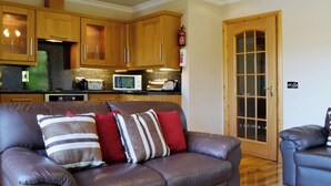 A living room with a leather sofa, wooden cabinets, a microwave, and a door with glass panels. - 1 bedroom accommodation in Achaphubuil near Fort William (Achaphubuil near Fort William)