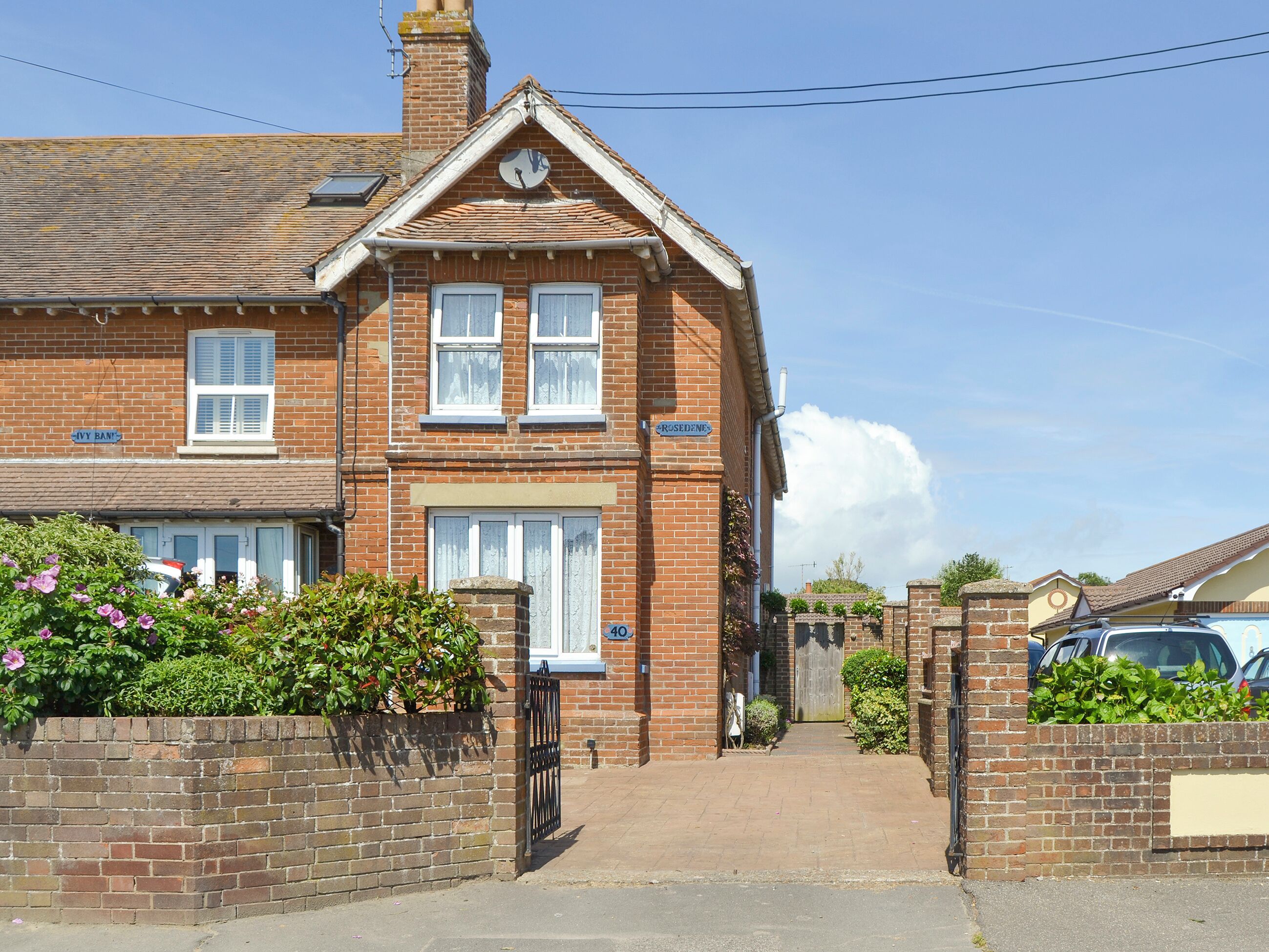 A two-story brick house with a front garden, a gate, and a clear sky.