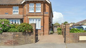 Une maison à deux étages, construite en briques, avec un jardin devant, une porte et un ciel dégagé.