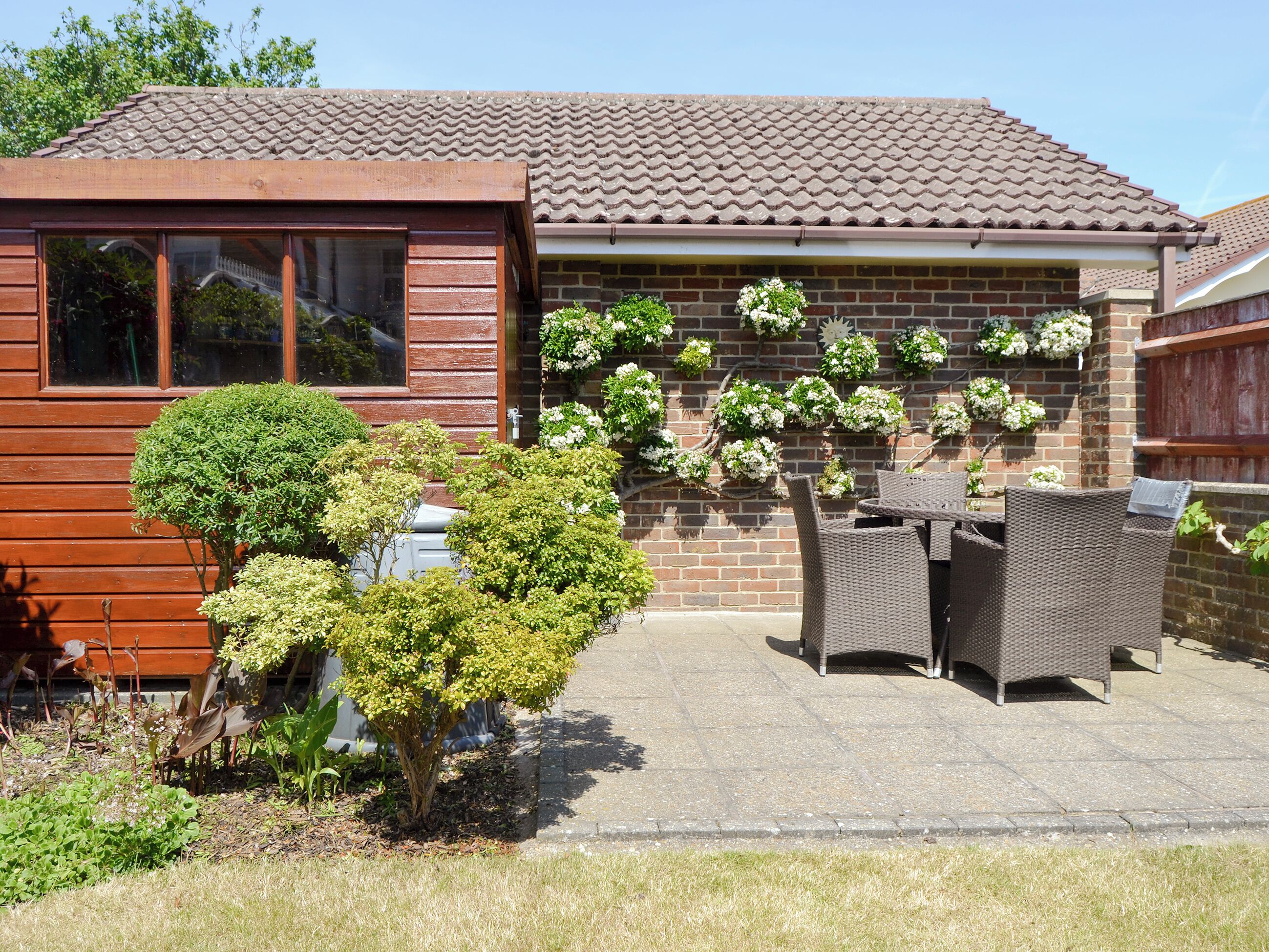 A residential house with a tiled roof, a brick wall, and a patio area with wicker furniture and potted plants.