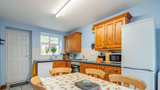 A kitchen with wooden cabinets, a white refrigerator, a microwave, and a dining table with chairs. - 3 bedroom accommodation in York (York)