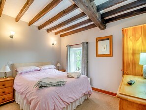 Un dormitorio con cama, lámparas de mesita, cabecera de madera, ventana con cortinas, un cuadro enmarco y una mesita de noche de madera con lámpara.